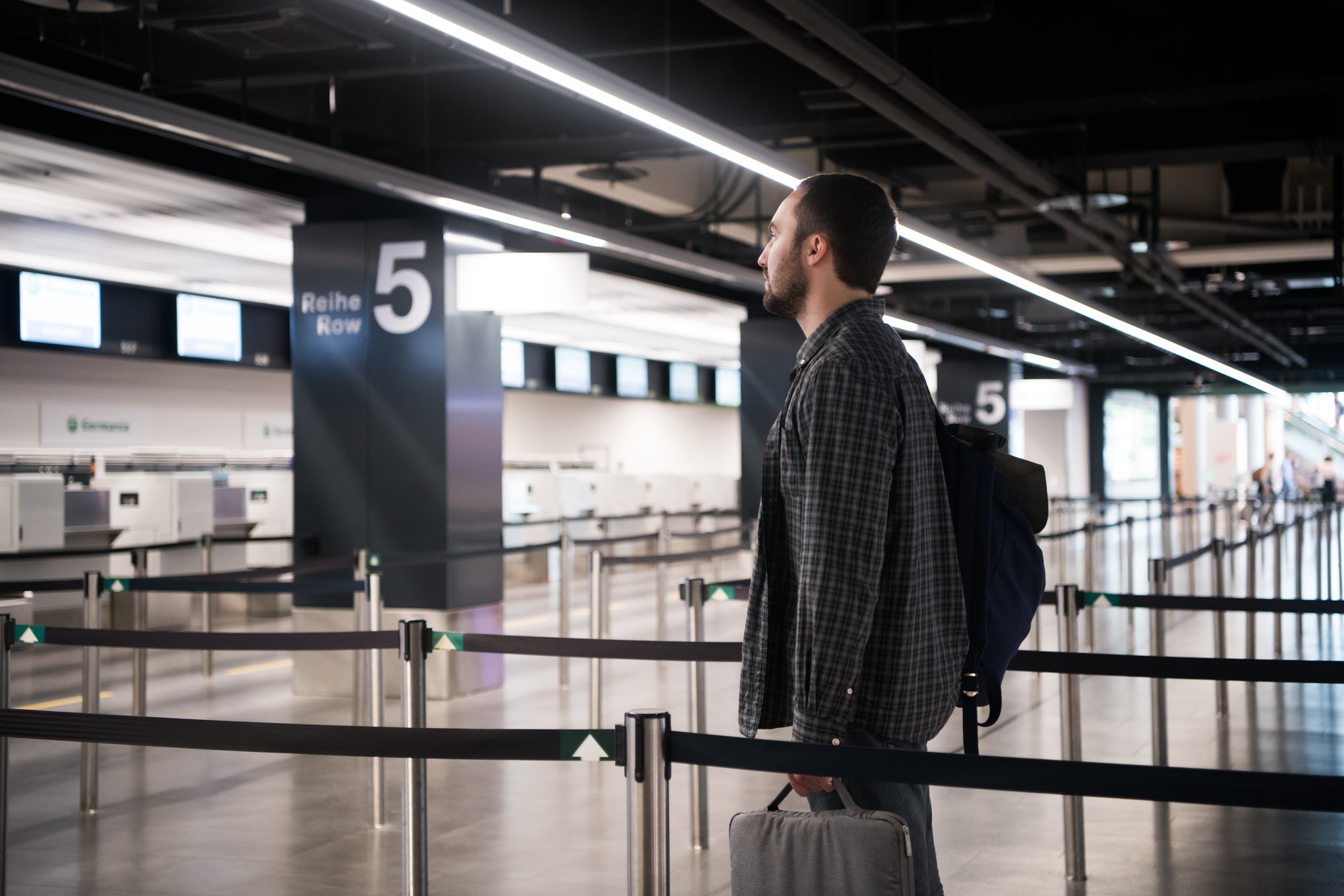 Young man with his luggage and backpack using smartphone while waiting for airline flight in the