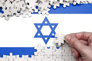 Israel flag is depicted on a table on which the human hand folds a puzzle of white color.