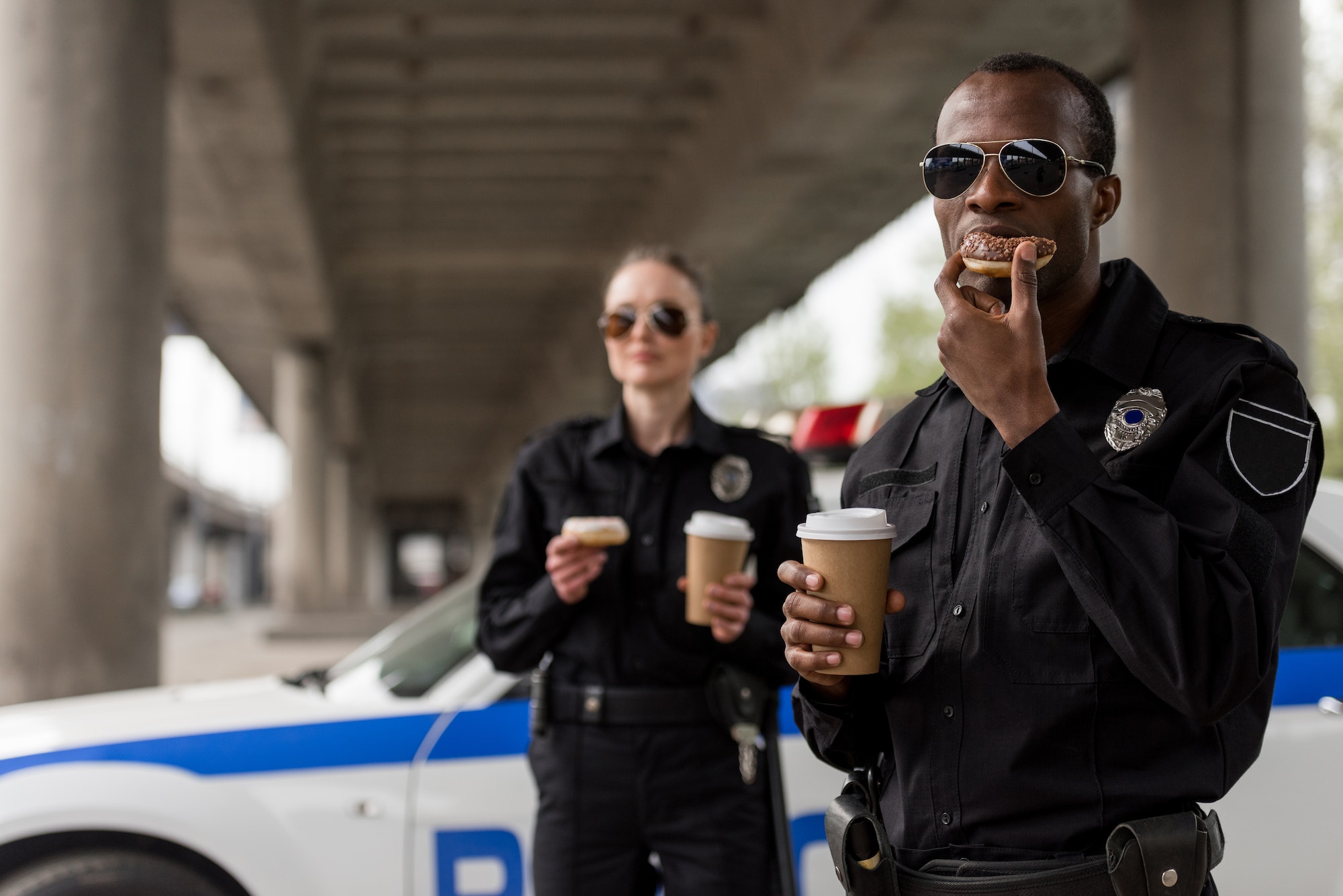 young police officers having coffee break with doughnuts in front of police car